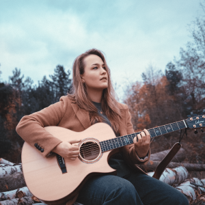 Sophie sitzt vor einem Herbstwald und spielt Gitarre