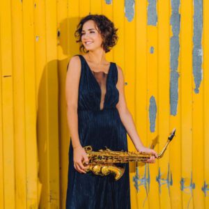 Asya Fateyeva ist im Porträt zu sehen während sie vor einer gelben Wand steht