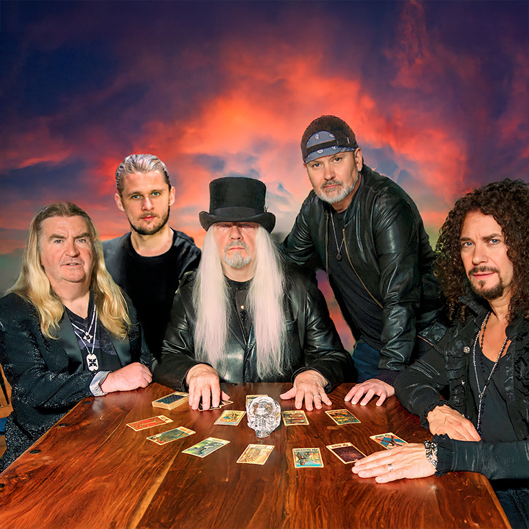 5 Männer in rockigen Klamotten rund um einen Tisch mit Spielkarten