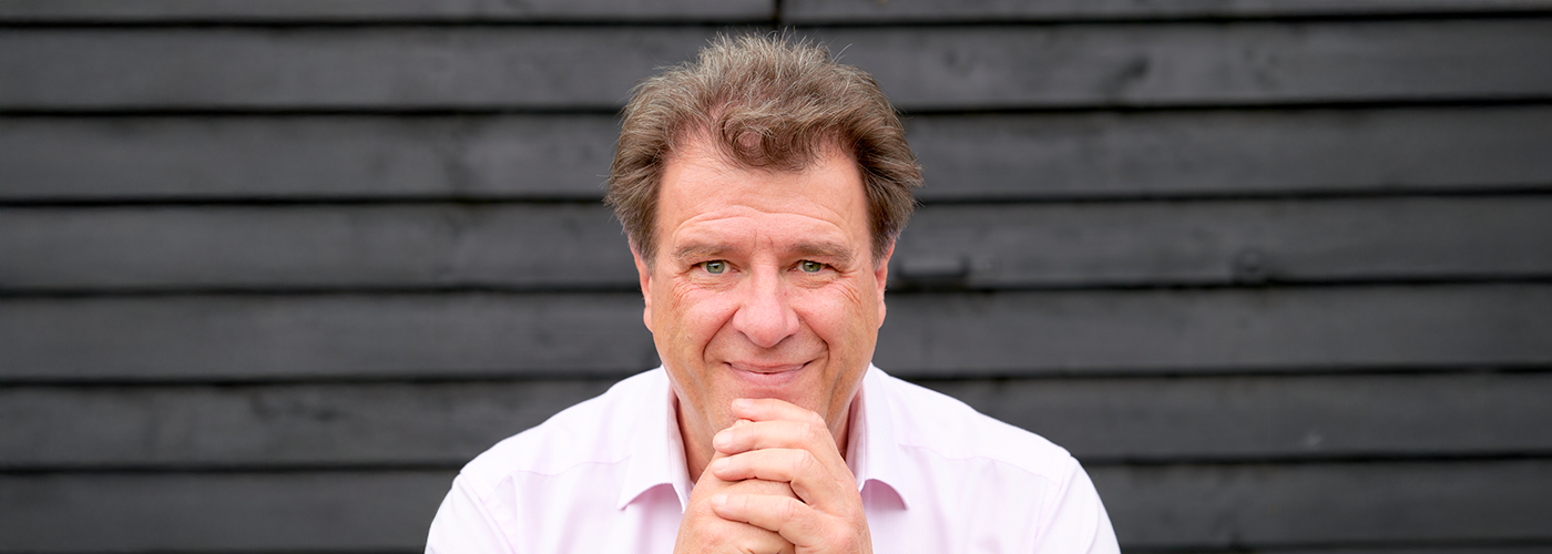 Portraitbild des Autors Alexander Schwarz. Schwarz trägt ein hell-rosa Hemd. Seine Hände sind vor dem Kinn gefaltet.