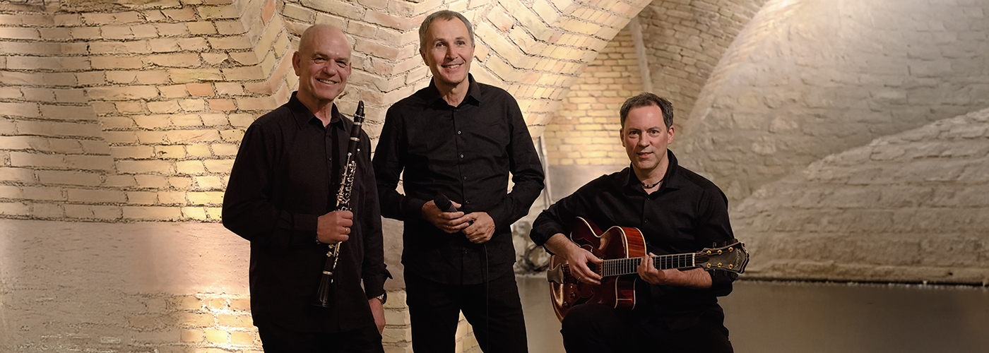 Die drei Künsterl des Brel-Trios stehen mit ihren Instrumenten im Gewölbekeller des Ingelheimer Winzerkellers. Sie tragen alle schwarze Kleidung.