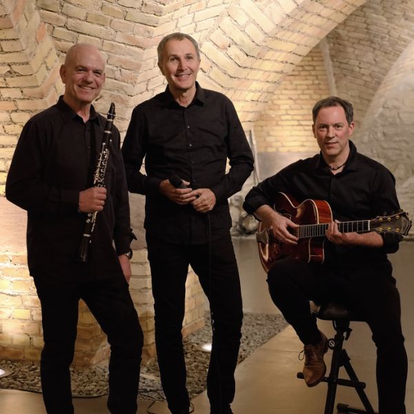 Die drei Künsterl des Brel-Trios stehen mit ihren Instrumenten im Gewölbekeller des Ingelheimer Winzerkellers. Sie tragen alle schwarze Kleidung.