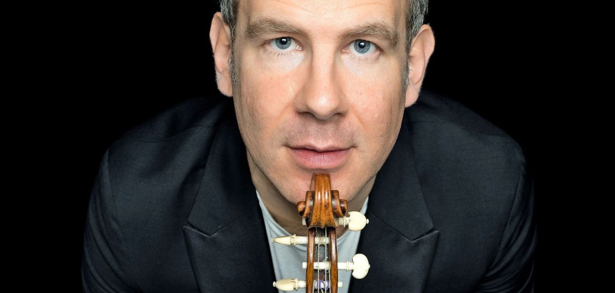 Portrait vo Johannes Pramsohler. An seinem Kinn lehnt eine Geige. Der Hintergrund ist schwarz