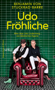 Buchcover "Udo Fröhliche" von Benjamin von Stuckrad Barre. Udo Lindenberg und Benjamin von Stuckrad-Barre sitzen auf einem rotbraunen Sessel vor einer grünen Wand.