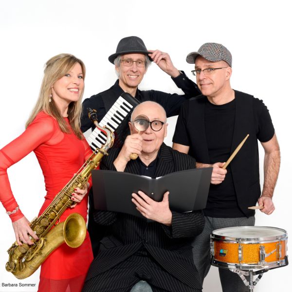 Das Bild zeigt Jo Jung und die Band Boogaloo. Es sind drei schwarzgekleidete Männer zu sehen und eine Frau in rotem Kleid. Die Band hat Instrumente in den Händen, Jo Jung ein Buch und eine Lupe.