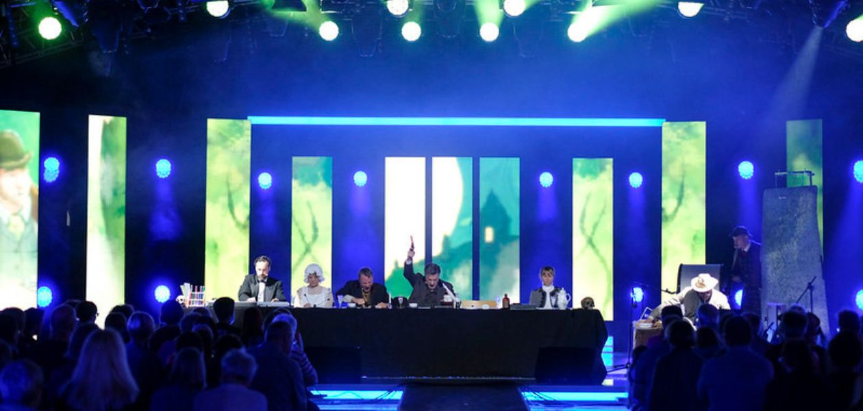 Das Ensemble des RadioLiveTheaters, verkleidet als Sherlock Holmes, vor beleuchtetem Hintergrund
